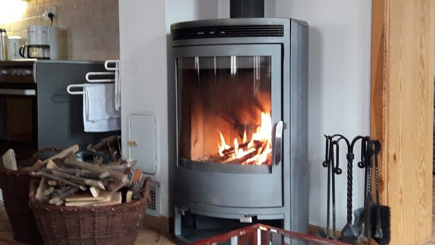 A wood-burning stove with a fire, a basket of firewood, and a kitchen area with a coffee maker and a toaster.