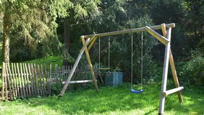 A wooden swing set in a grassy area with a wooden fence and trees in the background.