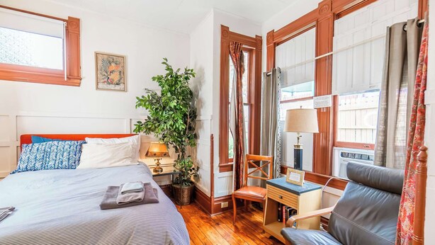 Una habitación de hotel con cama, escritorio, silla, planta en maceta y ventana con cortinas.