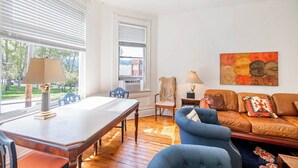 Una sala de estar con una mesa de comedor, sillones azules, un sofá marrón y un cuadro en la pared.