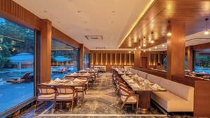 A restaurant with a long dining area, marble flooring, and large windows overlooking a pool area. - Tree of Life Amara Resorts & Spa Udaipur (Udaipur)