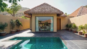 A pool area with a thatched-roof structure, potted plants, and a view of a mountainous landscape. - Tree of Life Amara Resorts & Spa Udaipur (Udaipur)