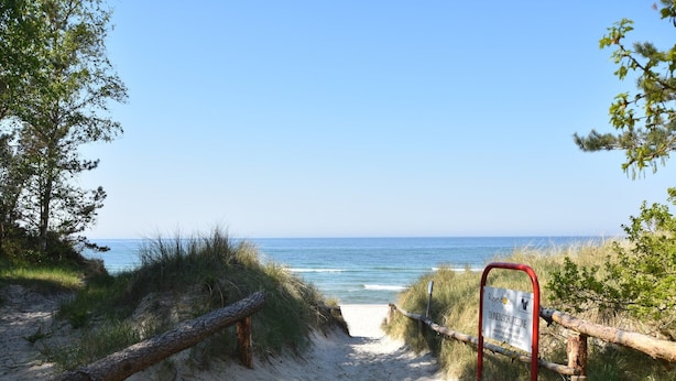 A sandy beach path leading to the ocean with a wooden fence and a sign indicating a dune protection zone. - Gemütlicher Aufenthalt am Wieker Hafen (Wiek auf Rügen)