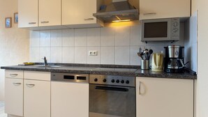 A modern kitchen with white cabinets, a built-in oven, a microwave, and a coffee maker. - Wohnung in Wiek nahe Juliusruh Strand (Wiek auf Rügen)