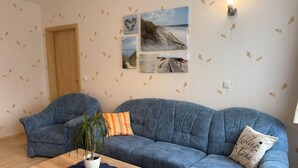 A living room with a blue sofa, a wooden coffee table, and a potted plant. - Wohnung in Wiek nahe Juliusruh Strand (Wiek auf Rügen)