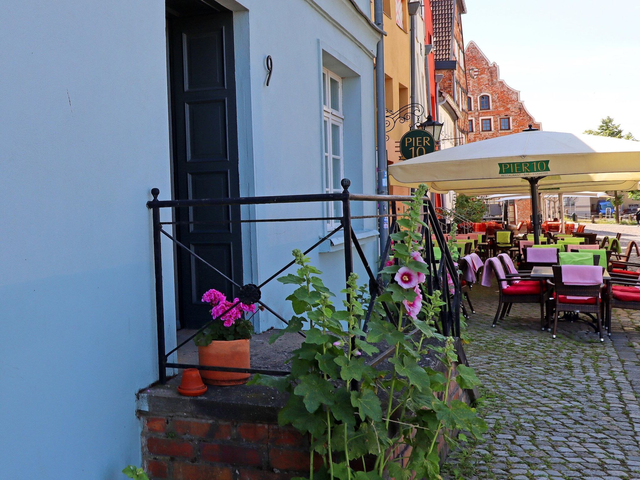 An outdoor caf é with tables and chairs, a brick wall, and a building with a sign that reads "PIER 10".