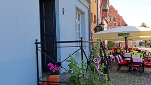 An outdoor café with tables and chairs, a brick wall, and a building with a sign that reads "PIER 10". - Wohnung in Wismar mit Garten (Wismar)