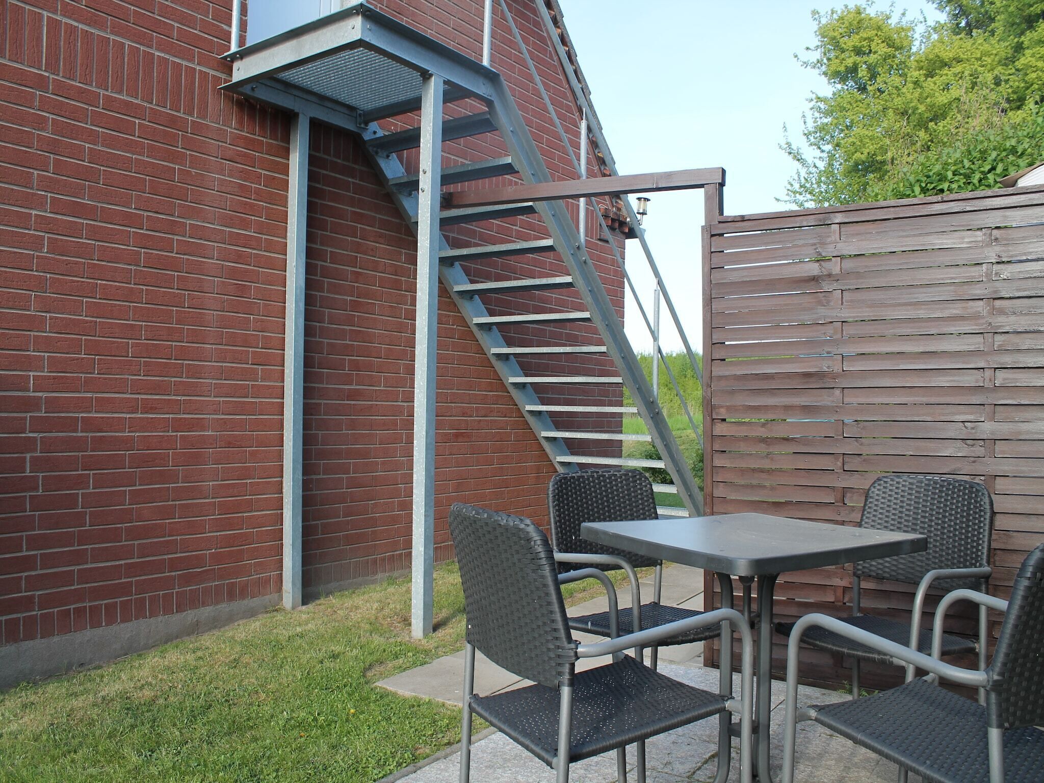 Eine Terrassenfläche mit einer Metalltreppe, zwei Metalltischen und vier Metallstühlen.