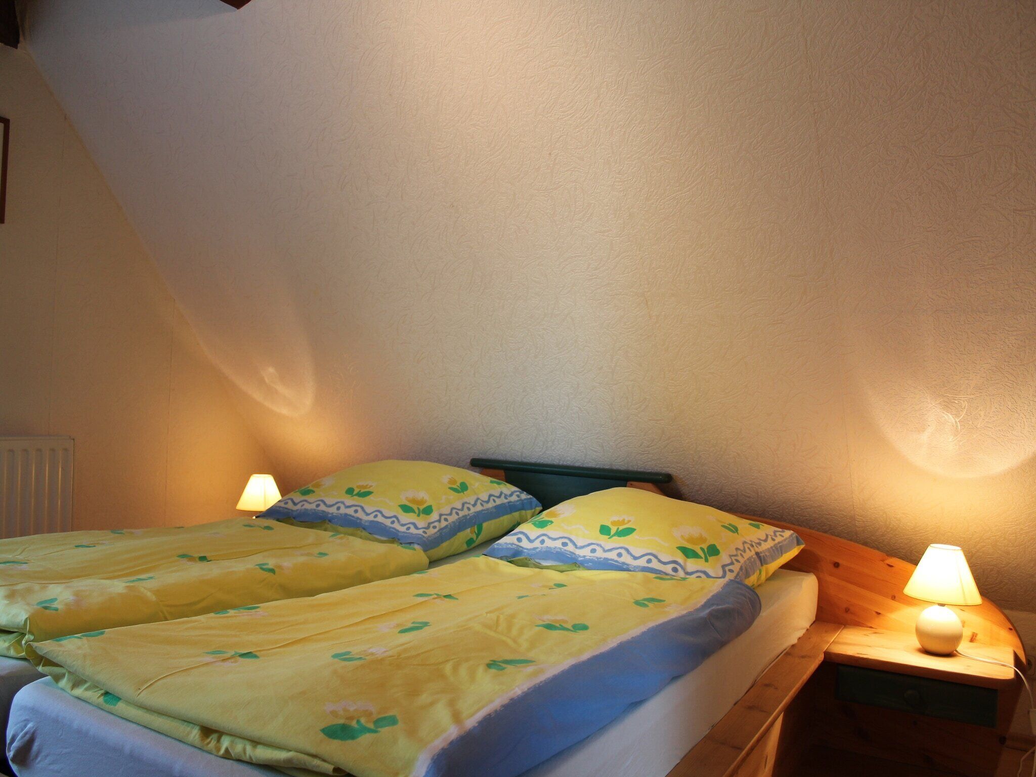 Ein Doppelbett mit floralem Bettzeug, zwei Nachttischlampen und ein Holznachttisch.