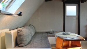 A cozy attic bedroom with a sloped ceiling, a white sofa, a wooden coffee table, and a view through a window. - Moderne Ferienwohnung in Meeresnähe in Tarnewitz (Boltenhagen (Ostseebad))