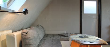 A cozy attic bedroom with a sloped ceiling, a white sofa, a wooden coffee table, and a view through a window.
