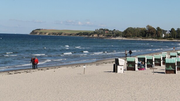 A beach with a sandy shore, a few people, and beach huts with striped awnings. - Moderne Ferienwohnung in Meeresnähe in Tarnewitz (Boltenhagen (Ostseebad))