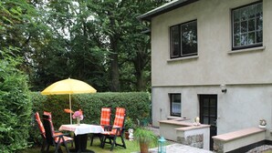 A patio with a table and chairs, a yellow umbrella, and a statue.