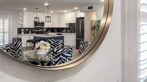 A modern kitchen with white cabinets, a central island, and a dining area with zebra-patterned chairs. - Home with Backyard Fun: Hot Tub, Golf, BBQ, Games! (Phoenix)