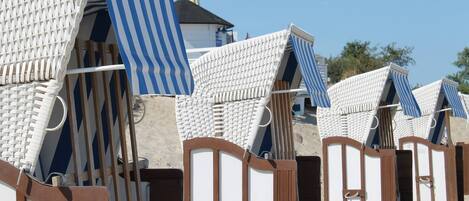 Strandhütten mit Streifenmarkisen und Holztüren, anordiniert in Reihen auf einem Sandstrand.