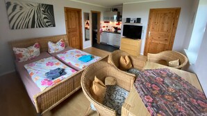 A room with a bed, two wicker chairs, a small table, and a TV. - Ferienwohnung in Bastorf for 3 Personen (Bastorf)