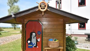 A wooden cabin with a red door, a ship's wheel, and a basket on a bench. - Ferienwohnung in Bastorf for 3 Personen (Bastorf)