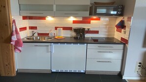 Een kleine keuken met witte kastjes, een roestvrijstalen spoelbak, een magnetron en een koffiezetapparaat.