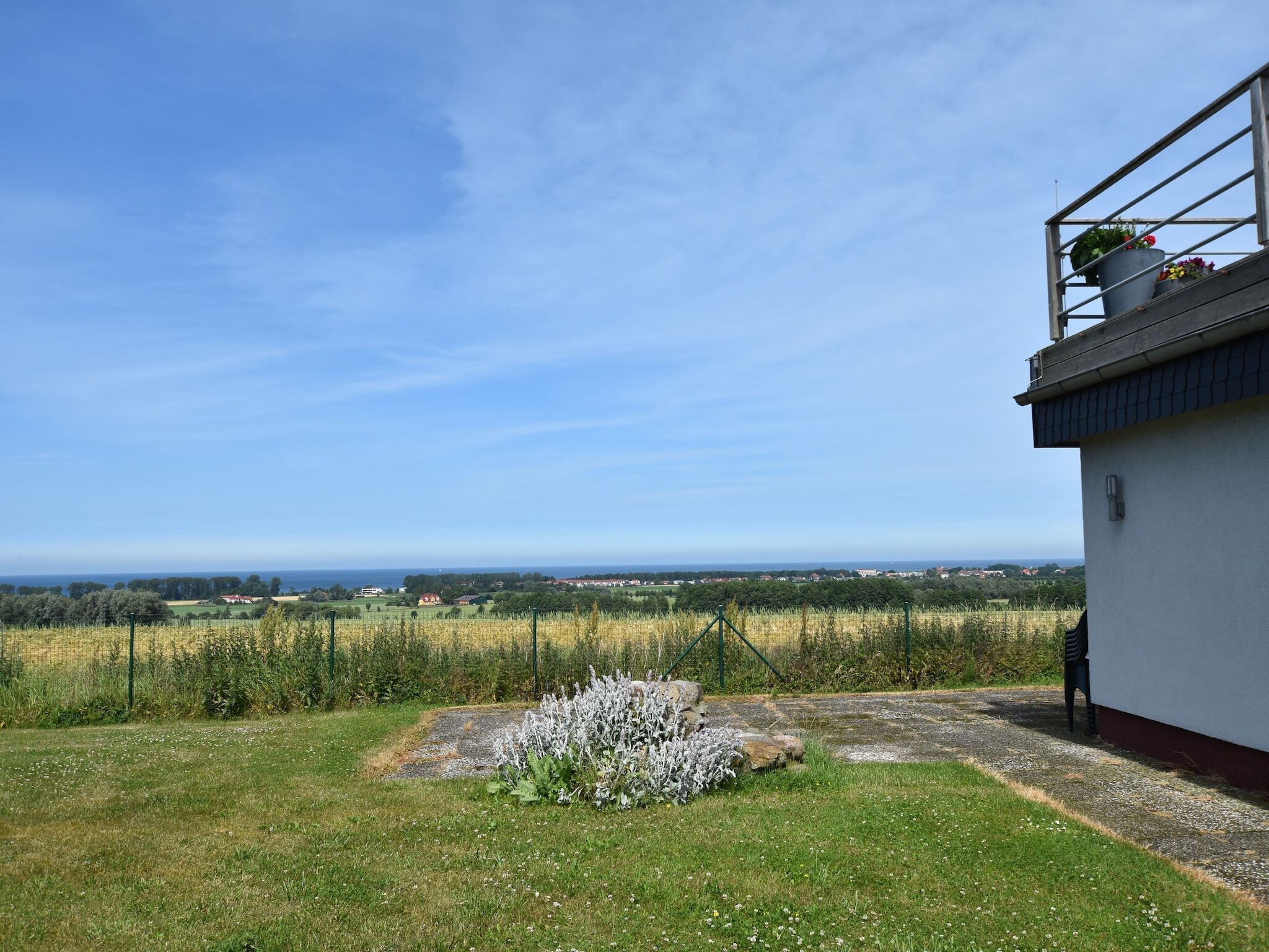 A white building with a balcony, a grassy yard, and a view of a distant landscape.