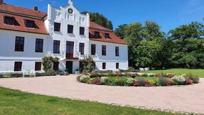 A white building with a red roof, multiple windows, and a garden in front. - Schicke Ferienwohnung in der Nähe der Ostseeküste (Gerdshagen)