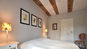 A bedroom with a large bed, a nightstand with a lamp, a chair, and three framed botanical prints on the wall. - Schicke Ferienwohnung in der Nähe der Ostseeküste (Gerdshagen)