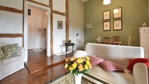 A living room with a white sofa, a coffee table with a vase of flowers, wooden flooring, and a green wall with framed pictures. - Wohnung nahe Ostsee Kühlungsborn (Gerdshagen)