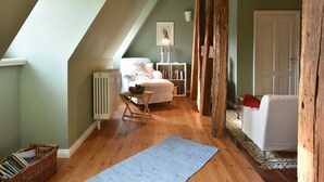 A cozy attic bedroom with a sloped ceiling, a white sofa, a small table with a bowl of fruit, a radiator, and a wooden beam structure. - Wohnung nahe Ostsee Kühlungsborn (Gerdshagen)