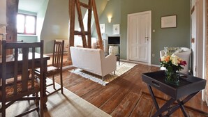 A cozy living room with wooden floors, a white sofa, a dining table with chairs, and a black side table with a vase of flowers. - Wohnung nahe Ostsee Kühlungsborn (Gerdshagen)