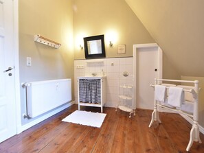 A bathroom with a white radiator, a sink with a mirror above it, a towel rack, and a shelf unit. - Wohnung nahe Ostsee Kühlungsborn (Gerdshagen)