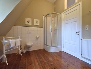 A bathroom with a wooden floor, a white toilet, a glass shower enclosure, and a white towel rack. - Wohnung nahe Ostsee Kühlungsborn (Gerdshagen)