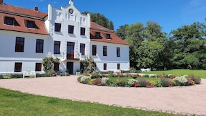 Un grande edificio bianco con tetto in tegole rosse, numerose finestre e un ingresso centrale.