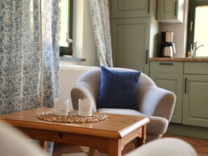 A cozy living room with a wooden coffee table, a patterned sofa, and a blue pillow. - Wohnung in Dargun, Mecklenburg mit Schwimmbad (Barlin)