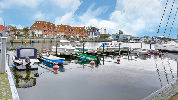 A marina with various boats docked, a building with a red roof, and a clear sky. - Modernes Appartement mit Terrasse auf Rügen (Wiek auf Rügen)
