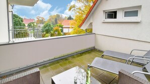 An outdoor patio with wicker furniture, a table with a bottle and glasses, and a view of houses and trees. - Modernes Appartement mit Terrasse auf Rügen (Wiek auf Rügen)