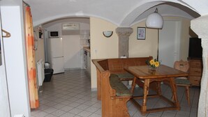 A dining area with a wooden bench and table, a kitchen in the background, and a white ceiling. - Wohnung in Weibig mit Garten (Struppen)