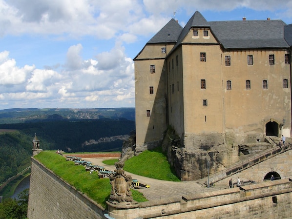 A historic castle with a prominent tower, a fortified wall, and a scenic view of the surrounding landscape.