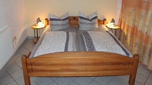 A neatly made bed with a wooden frame, two bedside lamps, and a floral painting on the wall. - Wohnung in Weibig mit Garten (Struppen)