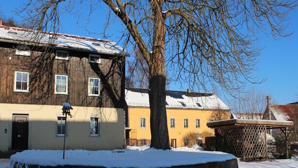 A wooden house with a snow-covered roof and a stone wall in front. - Wohnung in Weibig mit Garten (Struppen)