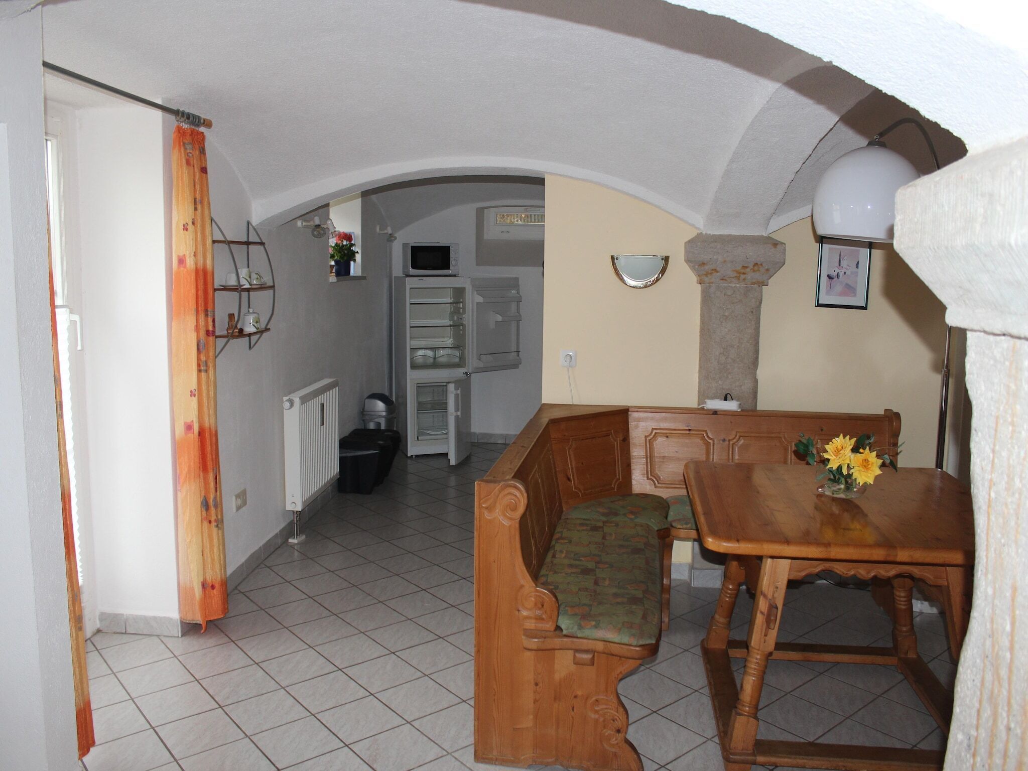 A compact kitchen with a wooden bench and table, a refrigerator, and a microwave.