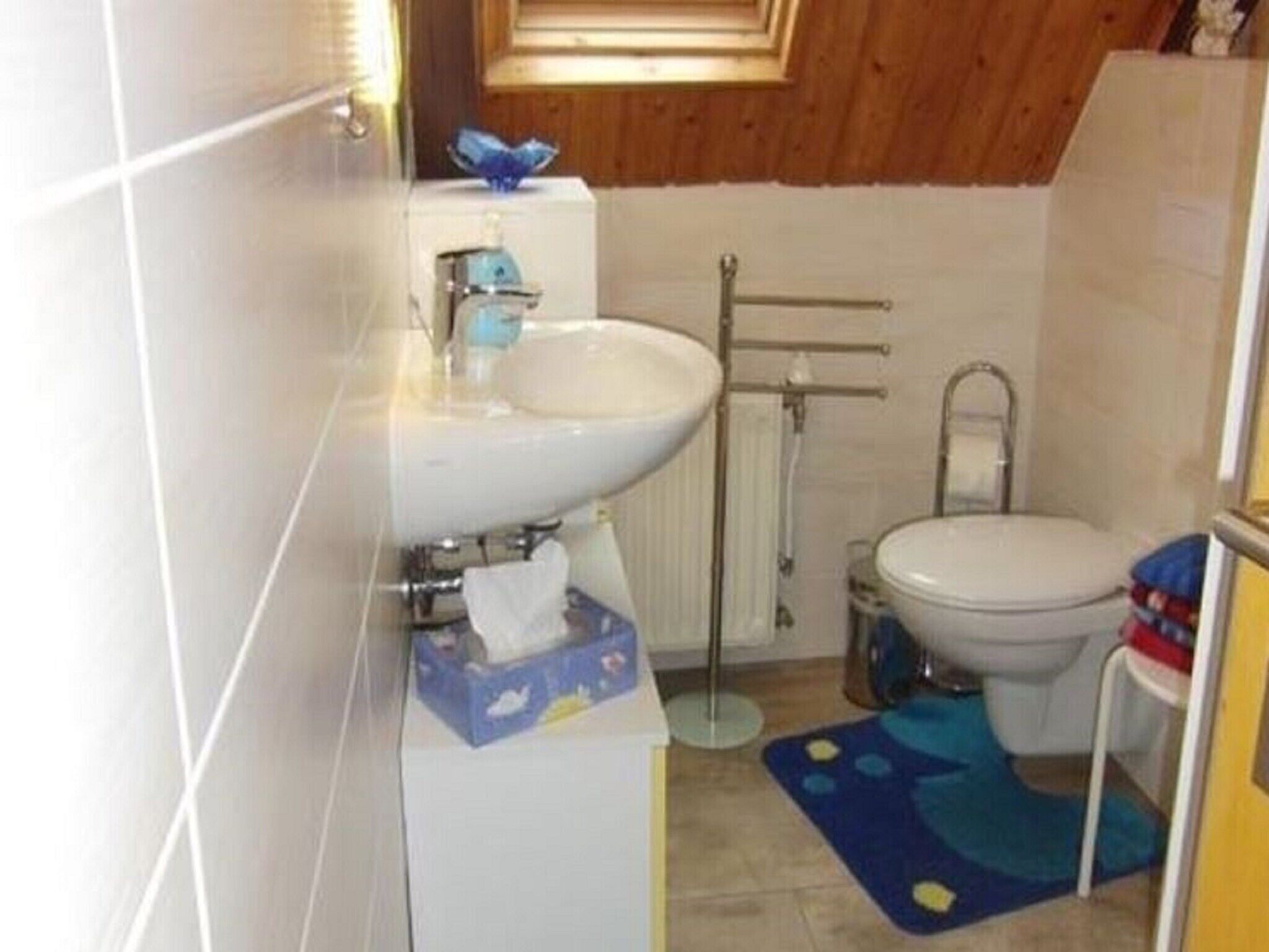 Et lille badeværelse med en hvid vask, toilet og en blå måtte på gulvet.