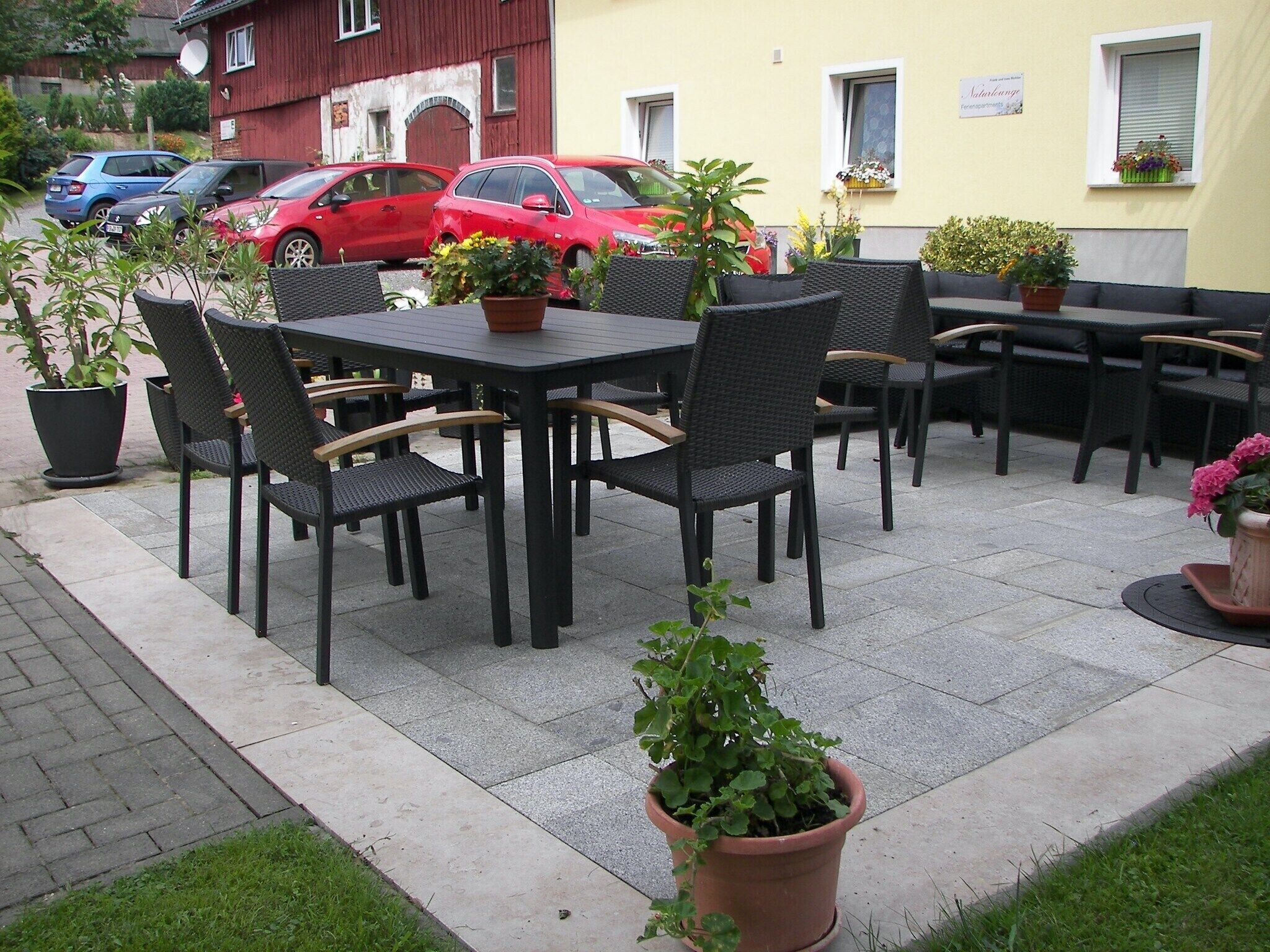 Un espace extérieur aménagé en terrasse, avec des tables et des chaises, entouré de plantes en pot.