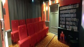 En teatersal med røde sæder, et mønstret tæppe og en reol med DVD'er.