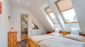 Une chambre avec deux lits, un plancher en bois, un puits de lumière et un radiateur.