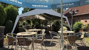 An outdoor seating area with tables and chairs under a large tent with a logo.