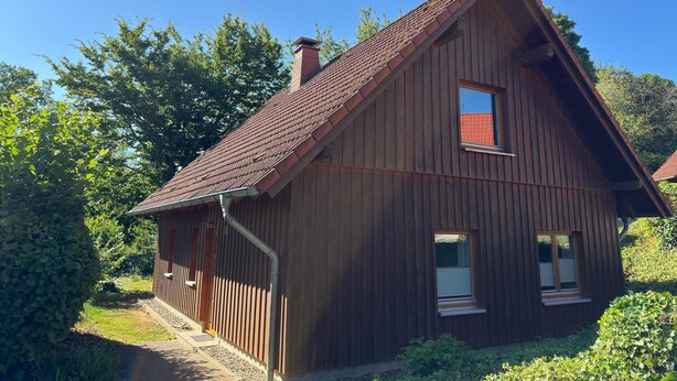 Una casa de madera con techo inclinado, una chimenea y un ventanal pequeño.