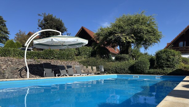 A swimming pool with lounge chairs and an umbrella.