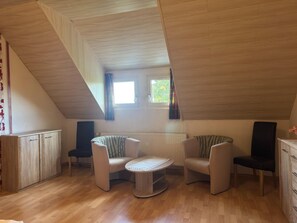 A cozy attic room with a sloped ceiling, wooden flooring, a round table, two sofas, and a cabinet.