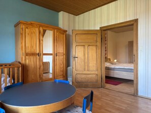 A room with a round table, wooden wardrobe, and a bed.