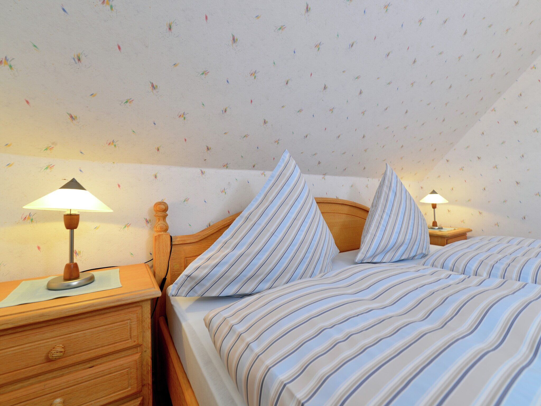 Un dormitorio con dos camas, ropa de cama a rayas, cabeceros de madera, lámparas de noche y un aparador.