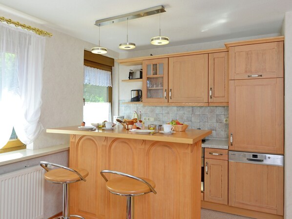 A kitchen with wooden cabinets, a central island with stools, and a built-in dishwasher. - Wohnung mit Garten in Eimelrod (Willingen-Eimelrod)